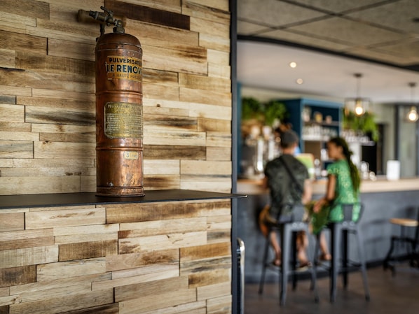 Ein Kupfer-Feuerlöscher an einer Holzwand, im Hintergrund eine Bar.