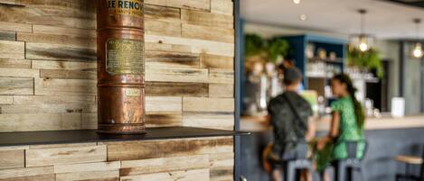 Un extintor de cobre montado en una pared de madera, con una zona de bar al fondo.