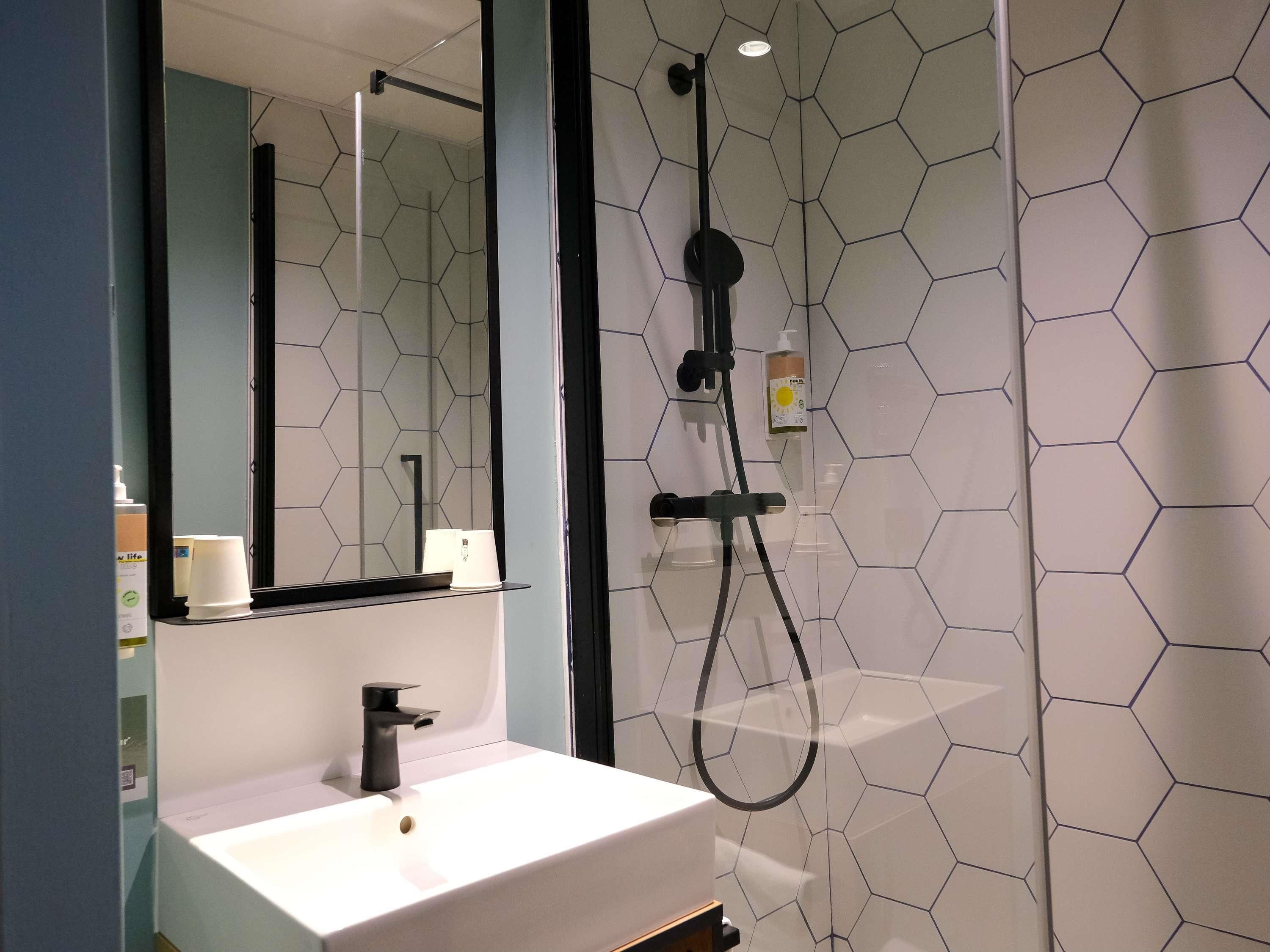 Een moderne badkamer met een witte wastafel, een spiegel en een douche met een zwarte doucheslang.