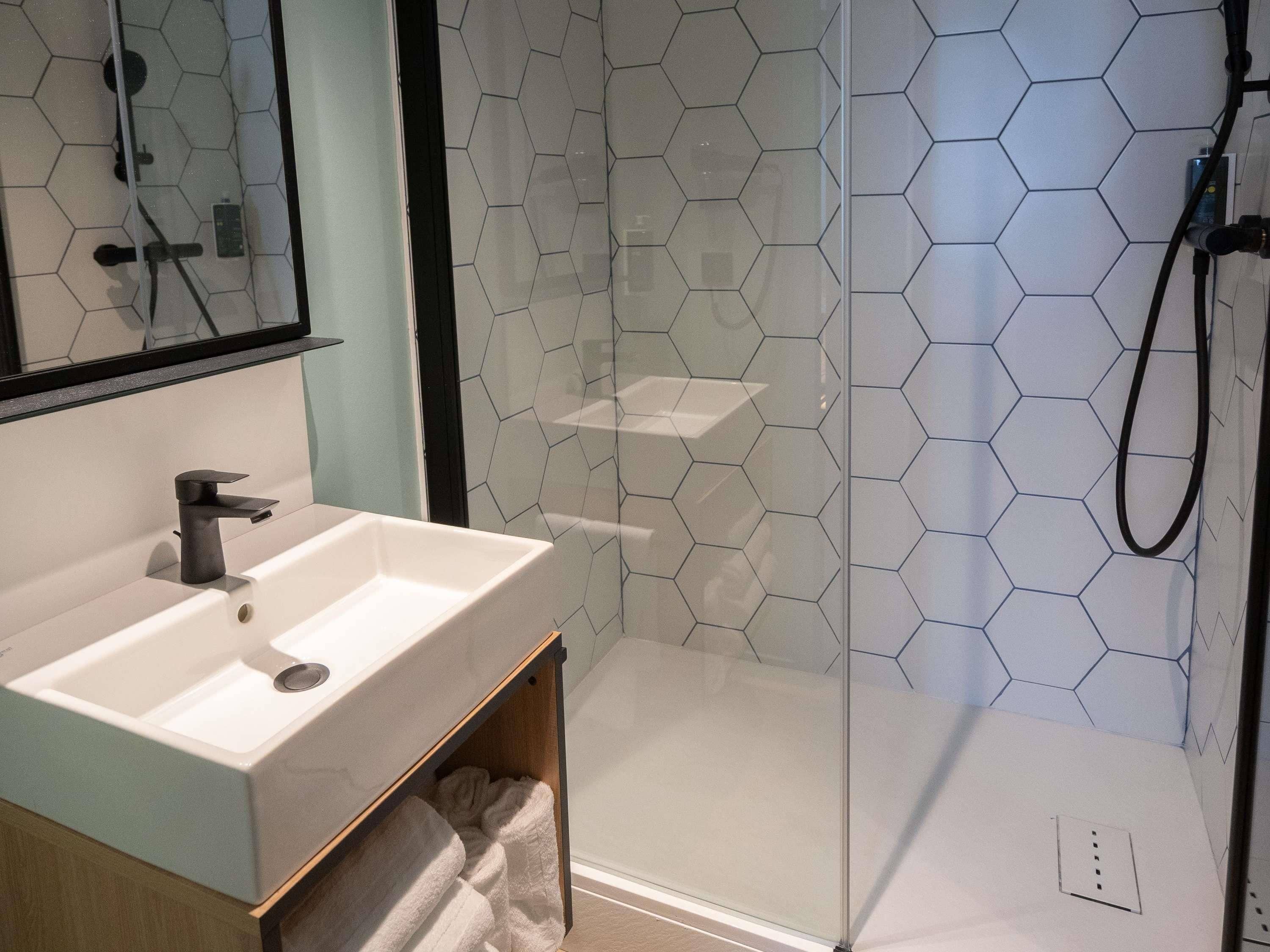 A modern bathroom with a white sink, a mirror, and a glass shower enclosure.