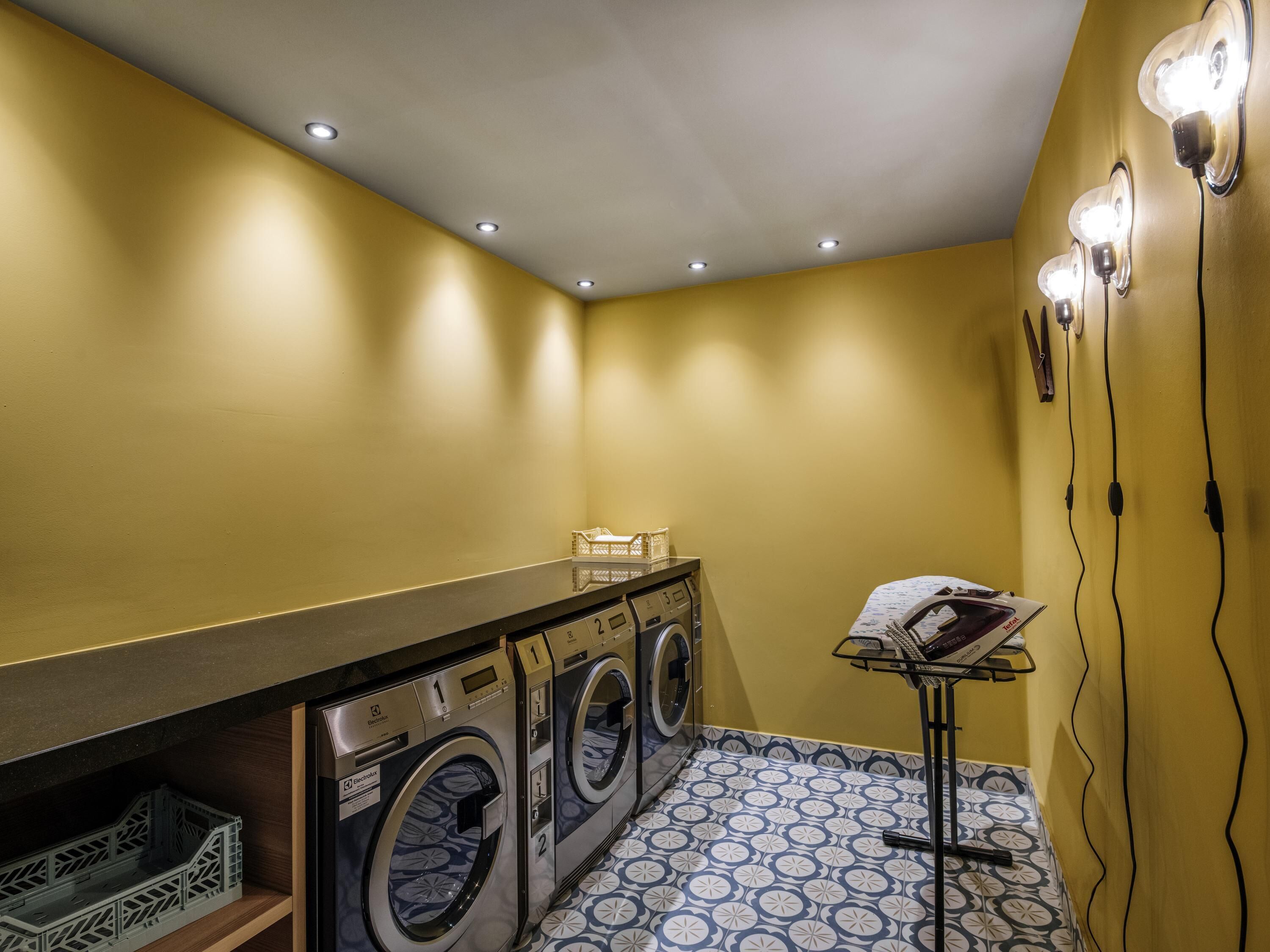 A laundry room with three front-loading washing machines, a drying rack, and a tiled floor.