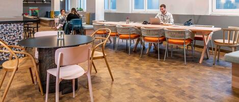 Un espace de restauration moderne avec des tables rondes, des chaises et des luminaires suspendus.