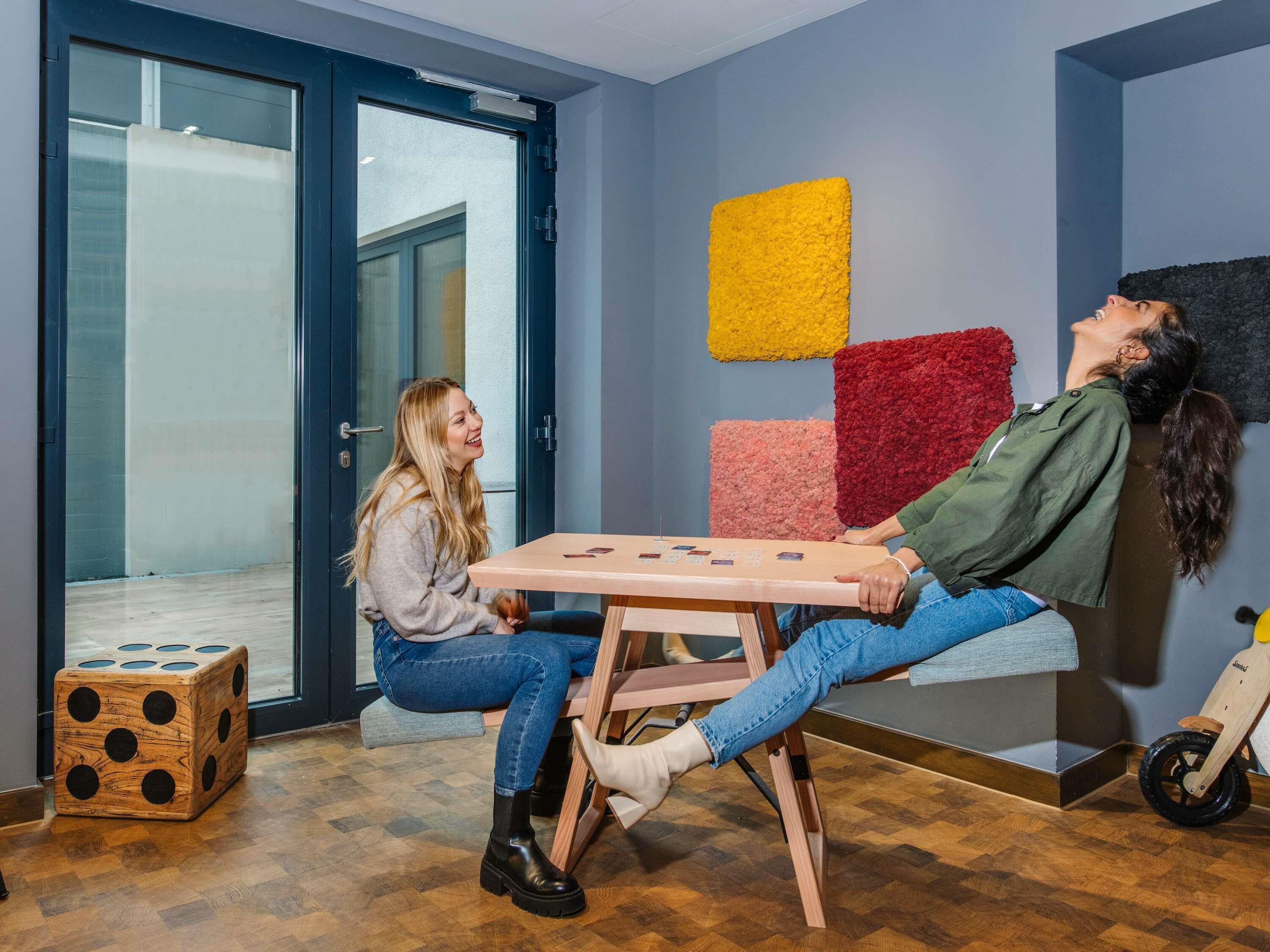 A room with a wooden floor, a table with cards, a dice, and colorful wall art.
