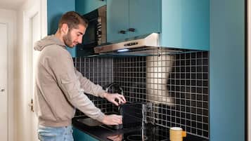 Une personne utilise un four dans une cuisine dont les armoires sont de couleur turquoise et le dosseret est recouvert de carreaux noirs.