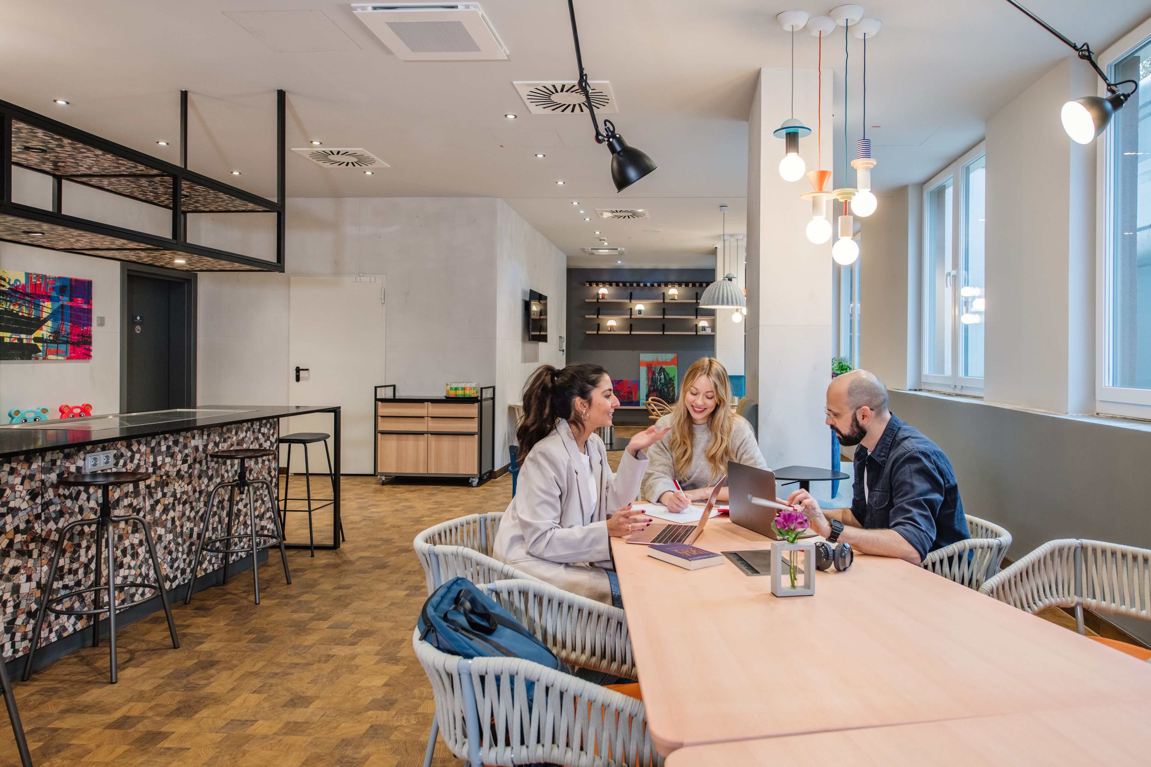 A modern kitchen with a bar area, white wicker chairs, and a long wooden table.