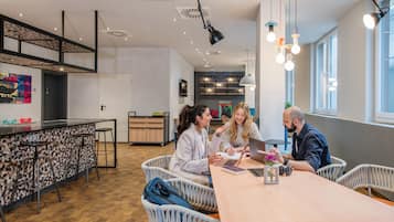 A modern kitchen with a bar area, white wicker chairs, and a long wooden table.