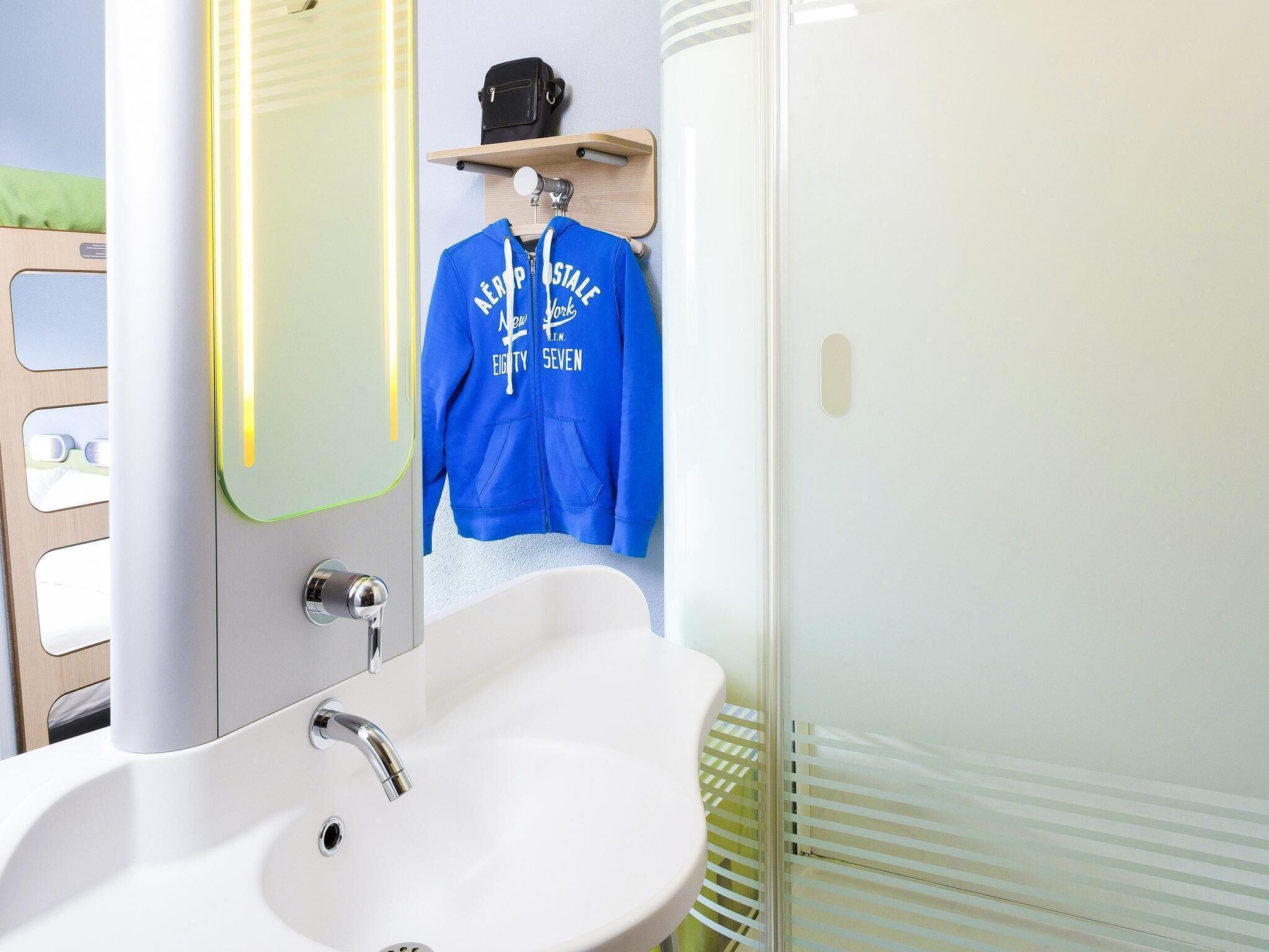 A bathroom with a white sink, a mirror, and a blue hoodie hanging on a rack.