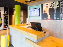 A reception desk with a computer monitor, a green pillar, and a wall with a poster.