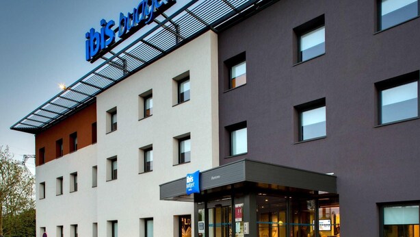 A modern hotel with a 'ibis budget' sign, a glass entrance, and a parking area with bollards. - ibis budget Montceau-les-Mines (Montceau-les-Mines)