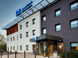 A modern hotel with a 'ibis budget' sign, a glass entrance, and a parking area with bollards.
