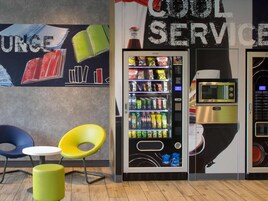 A vending machine with a microwave and a coffee machine, two chairs, and a wall with a 'Cool Service' sign.