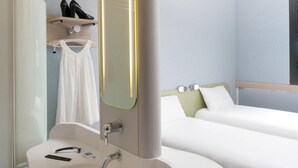 A hotel room with a white sink, a mirror, a bed with white bedding, and a shelf with shoes. - ibis budget Montceau-les-Mines (Montceau-les-Mines)