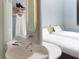 A hotel room with a white sink, a mirror, a bed with white bedding, and a shelf with shoes.