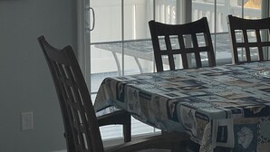 Een eethoek met een tafel bedekt met een geruit tafelkleed, twee houten stoelen en uitzicht op de oceaan door grote ramen.