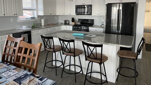 Een moderne keuken met witte kastjes, een roestvrijstalen koelkast, een gasfornuis en barstoelen.