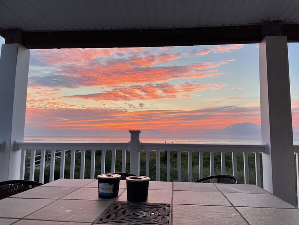 Un espace extérieur abrité, avec une table et des chaises, d’où l’on peut admirer le coucher de soleil sur l’océan.