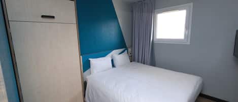 Een slaapkamer met een bed, een kledingkast, een raam met gordijnen en een plafondlamp.