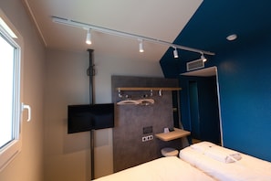 Habitación de hotel con cama, televisor montado en la pared, zona de ducha y pared decorativa azul.