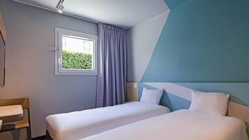 Une chambre d’hôtel avec deux lits, une fenêtre avec des rideaux, un bureau et une vue sur la verdure.