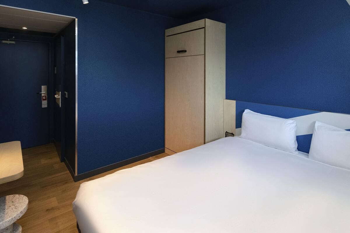 A hotel room with a large bed, a wardrobe, a desk, and a chair.