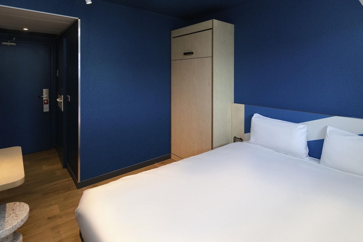 Hotellihuone, jossa on suuri sänky, vaatekaappi, työpöytä ja tuoli.