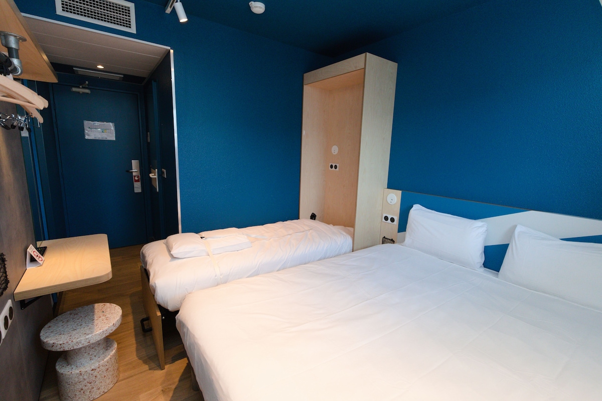 Habitación de hotel con dos camas, un escritorio pequeño y un cubo de basura.