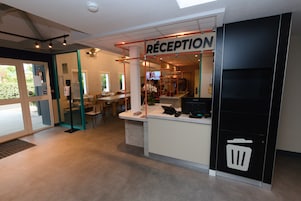 Zona de recepción con mostrador, un basurero y un área de descanso con sillas y una mesa.