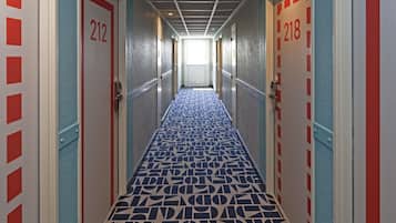 Un couloir avec un tapis à motifs, des portes numérotées 212 et 218, et un plafond orné d’un motif en réseau.