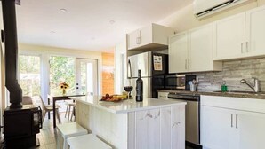 A modern kitchen with white cabinets, a central island, bar stools, and a wood-burning stove. - River House Getaway (Vienna)