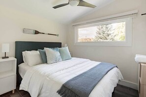 Quarto com cama, mesa de cabeceira, ventilador de teto, janela e vista para árvores.