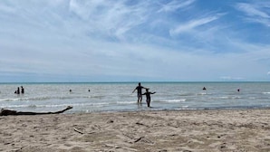 A beach with people in the water and on the sand, a clear sky, and a calm sea. - River House Getaway (Vienna)