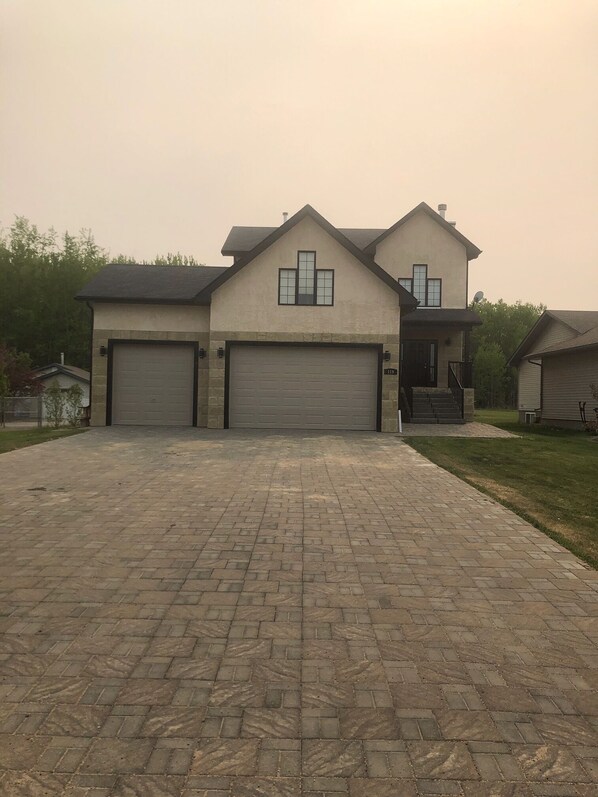 A two-story house with a brick driveway and two garage doors.