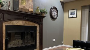 Un salon avec une cheminée, une table à manger avec des chaises, une horloge et un tableau encadré au mur.