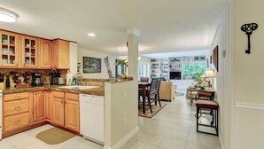 A kitchen with wooden cabinets, a dining area with a table and chairs, and a living area with a sofa and a lamp. - Newly remodeled! Upscale Condo on the World-renowned Amelia Island Plantation! (Fernandina Beach)