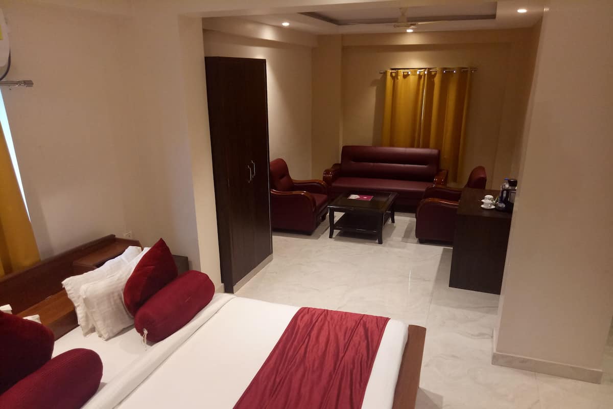A hotel room with a large bed, a sofa, a coffee table, and a desk with a chair.