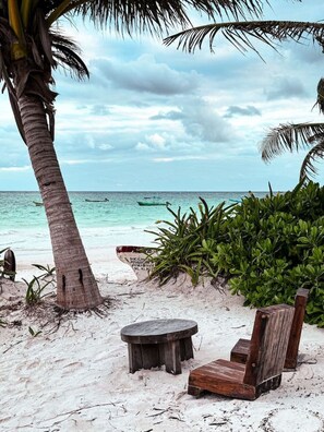 A beach with a wooden bench and a small table, surrounded by lush greenery and a palm tree. - IIK: A Hip Condo-Hotel Oasis in Tulum Centro (Tulum)