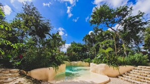 A circular hot tub surrounded by a stone wall, set in a garden with various plants and trees. - IIK: A Hip Condo-Hotel Oasis in Tulum Centro (Tulum)