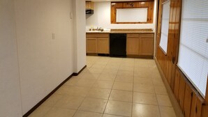 Una cocina con armarios de madera, lavavajillas y ventana con persianas.