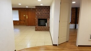 Una habitación amplia con suelo de baldosas, chimenea de ladrillo, puertas de madera y pared blanca.
