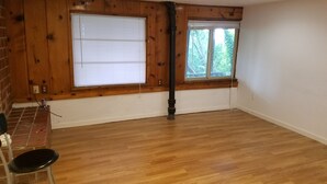 Una habitación con paneles de madera, un ventanal con persianas, piso de madera y una silla negra.