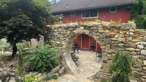 A red building with a stone archway leading to a stone patio. - Artistic barn: wood burning hottub, sauna and pizza oven  (Kent)