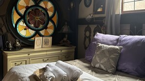 A bedroom with a bed, a dresser, a stained glass window, and a window with curtains. - Artistic barn: wood burning hottub, sauna and pizza oven  (Kent)