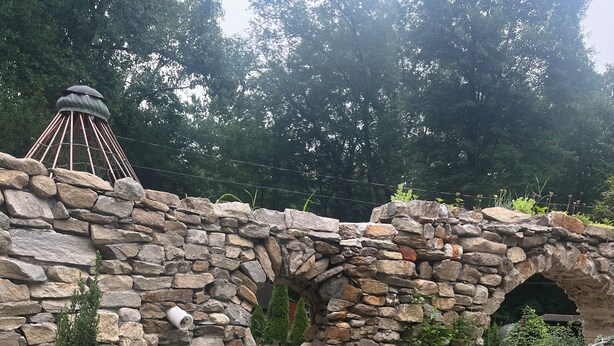 A stone archway leading to a patio area with a table and chairs. - Artistic barn: wood burning hottub, sauna and pizza oven  (Kent)