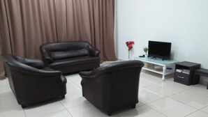 Una sala de estar con un sofá y dos sillones, un televisor sobre un mueble bajo, una pequeña mesa con una planta y un aparador.