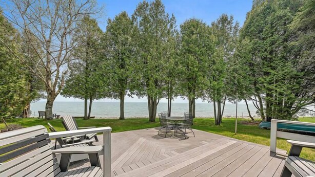 A deck with outdoor furniture, a table, and chairs, overlooking a body of water and surrounded by trees.