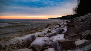 A rocky shoreline with ice formations and waves at sunset.