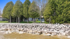 A riverbank with a rocky shoreline, a house with a porch, and several trees.