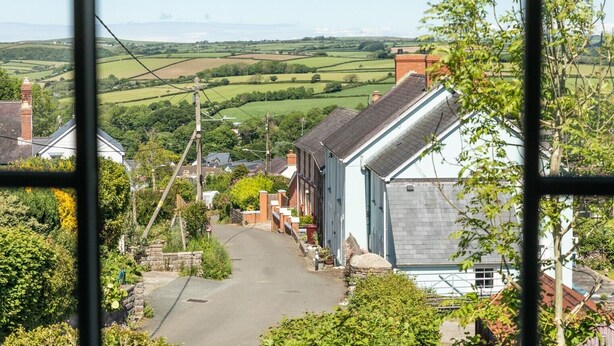 Une rue de campagne bordée de maisons, offrant une vue dégagée sur la campagne, et un panneau indiquant une limite de vitesse de 32 km/h.
