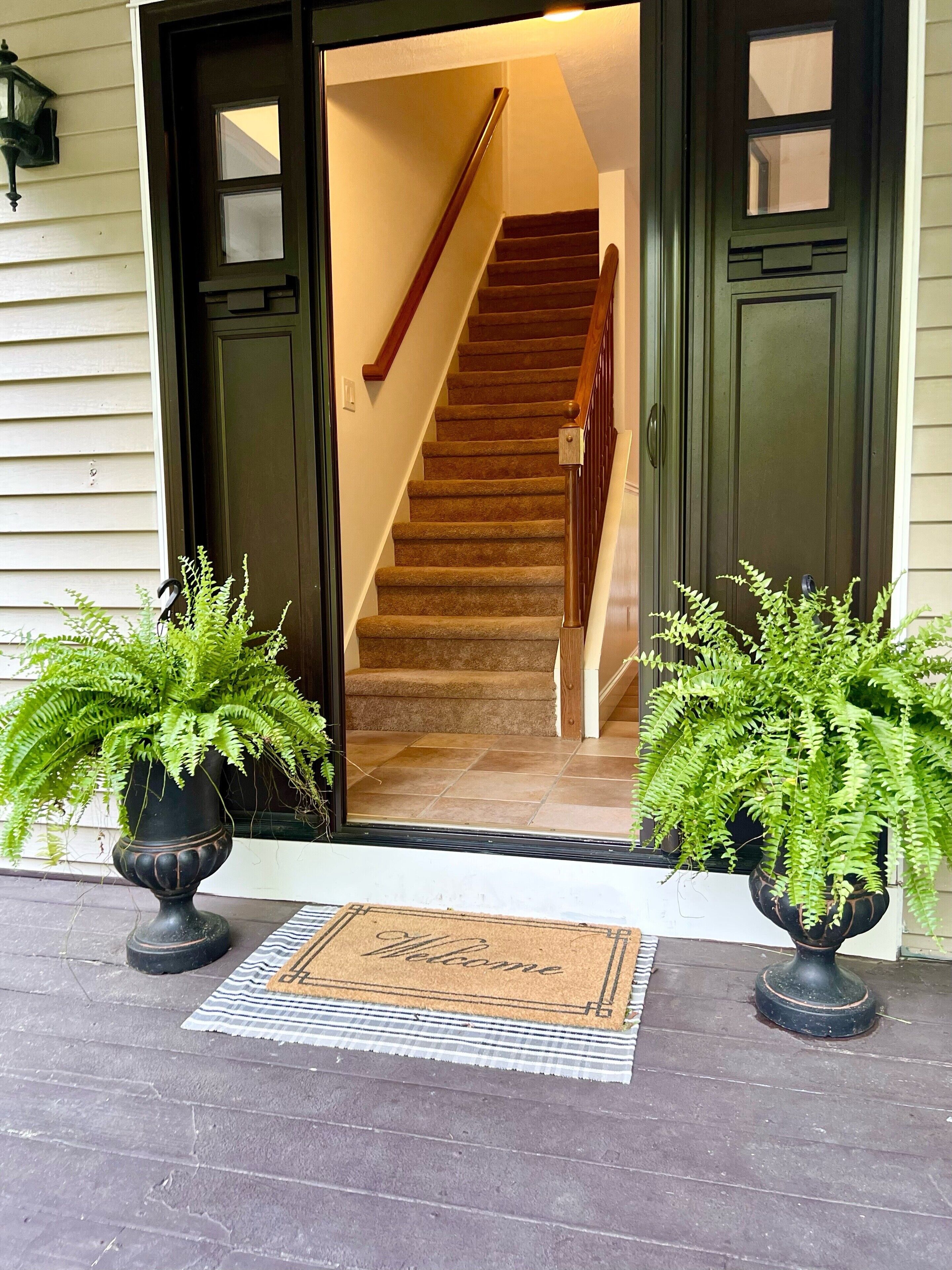 L’entrée de la maison est agrémentée d’un escalier en bois qui mène à l’intérieur. Deux fougères en pot sont placées de part et d’autre de l’entrée.