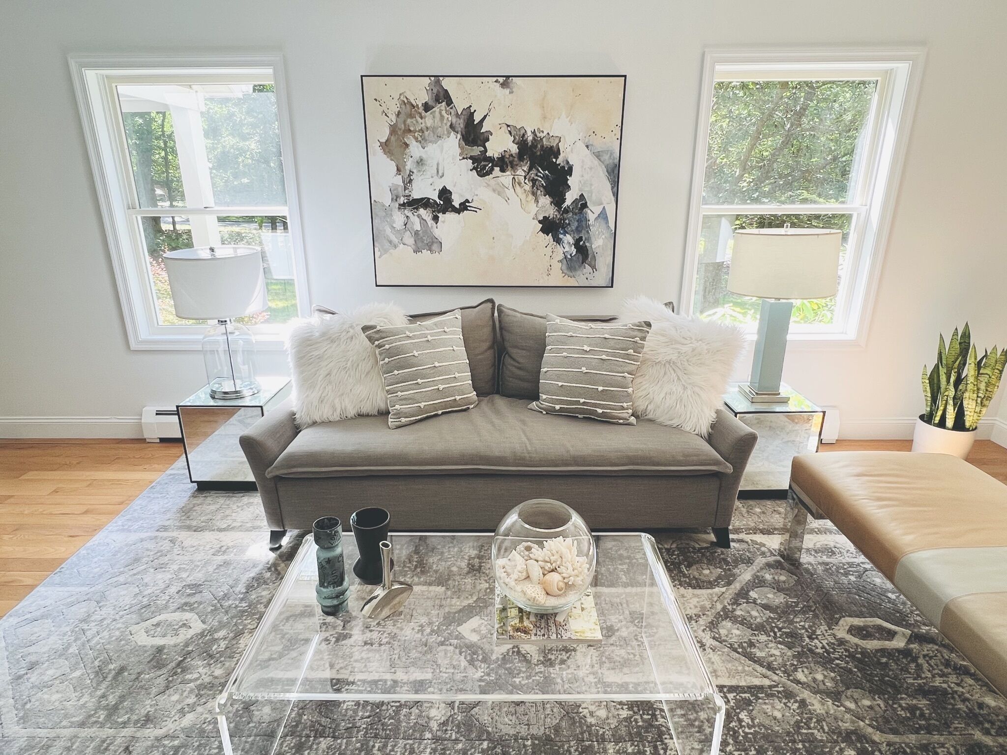 Un salon avec un canapé gris, une table basse en verre et un tableau accroché au mur.